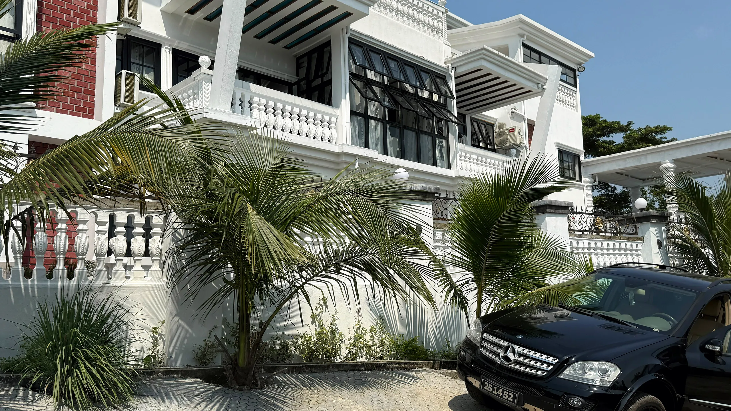 The white façade of the residence behind palm trees under a clear sky